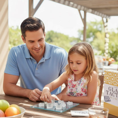 A man and a young girl sitting at a wooden table outdoors, playing with a small white game board.