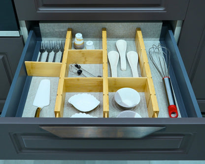 Expandable bamboo drawer dividers organising utensils, a whisk and small dishes in a grey kitchen drawer
